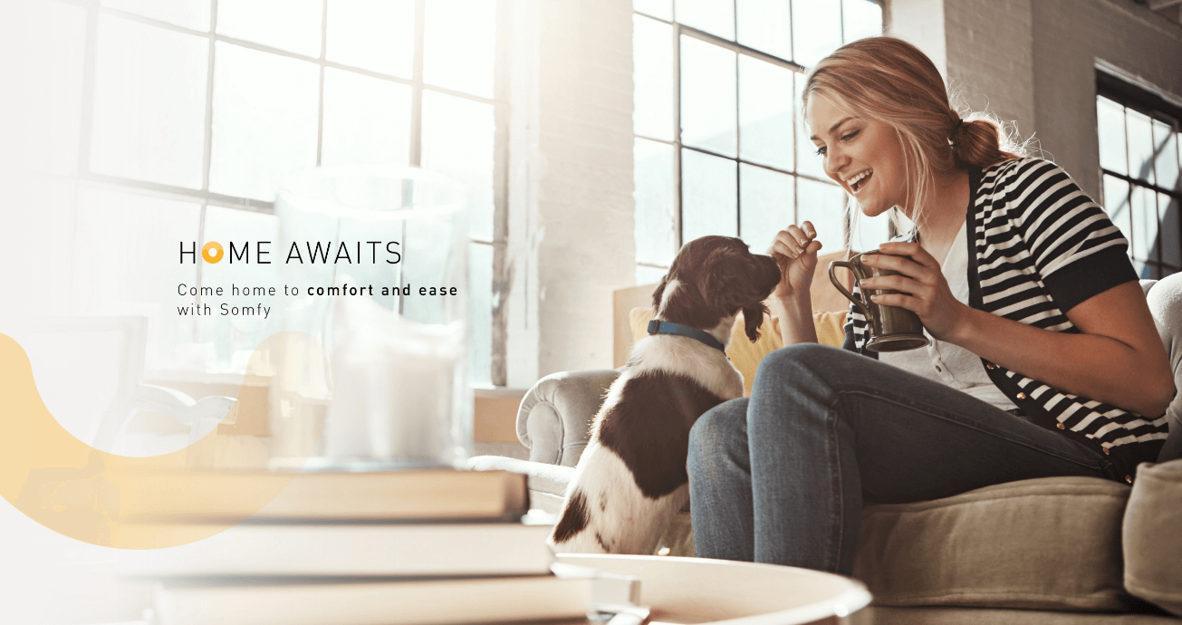 Campaign visual of a girl holding a coffee and bending down to interact with her dog whilst in her home with the campaign tagline home awaits